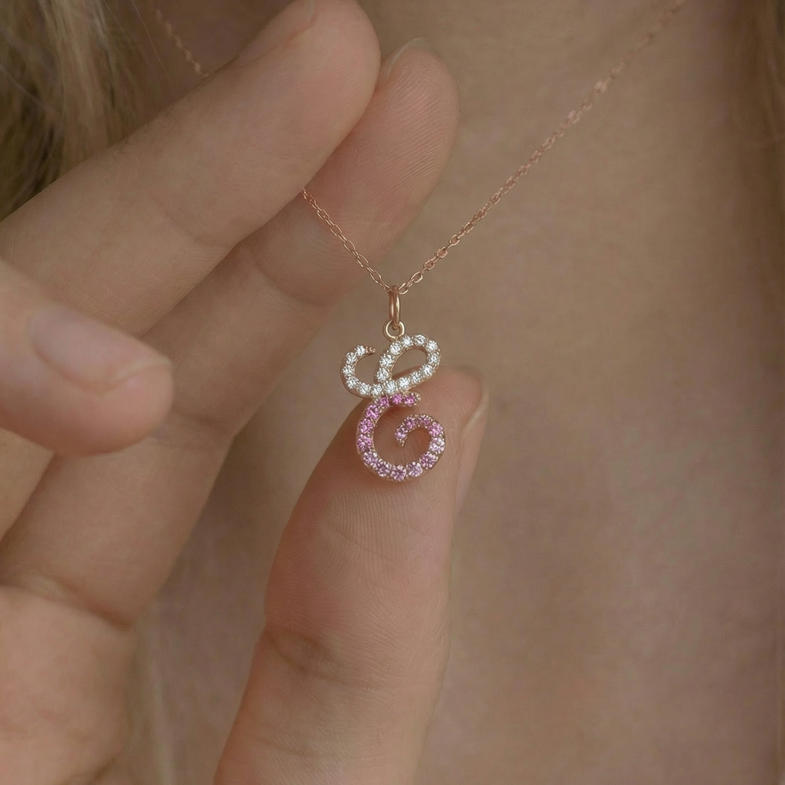 Close-up of a delicate necklace with a pink and white pendant held by a hand.